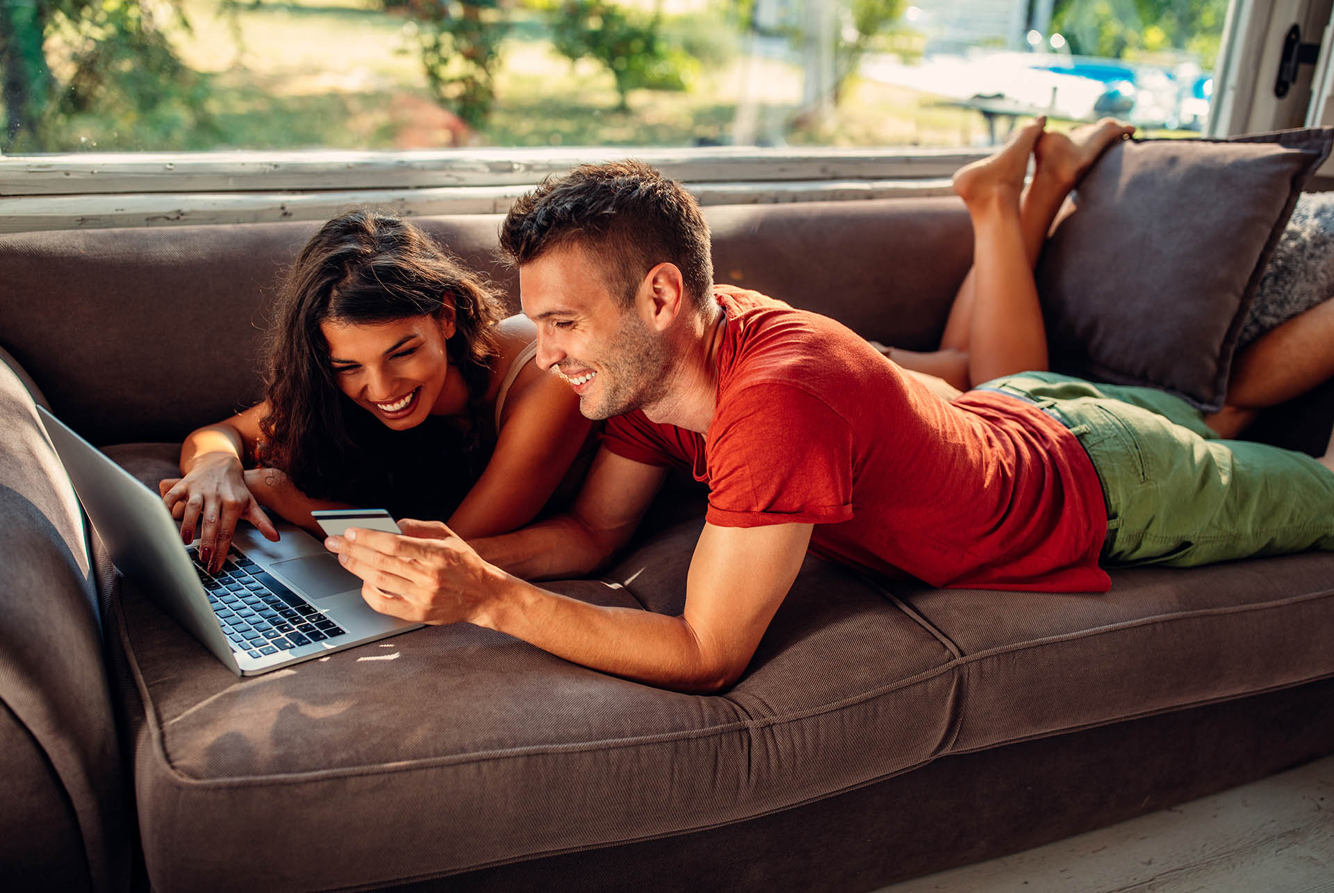 A couple using a laptop while lying on a sofa to shop online